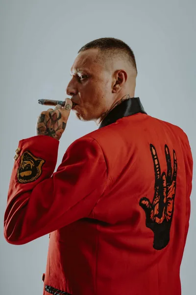 Inoki спиной в красном пиджаке с нарисованной на спине рукой, с сигарой во рту